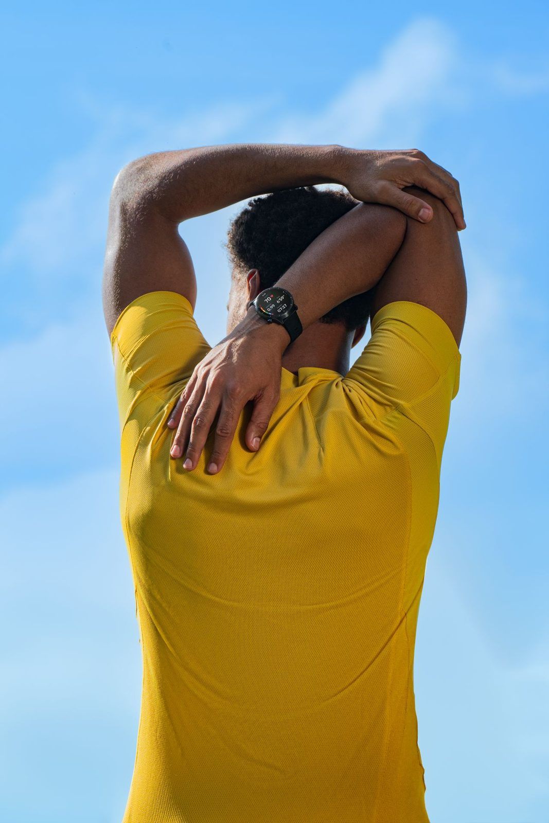 Un sportif de dos s’étire les bras au-dessus de la tête, montre au poignet