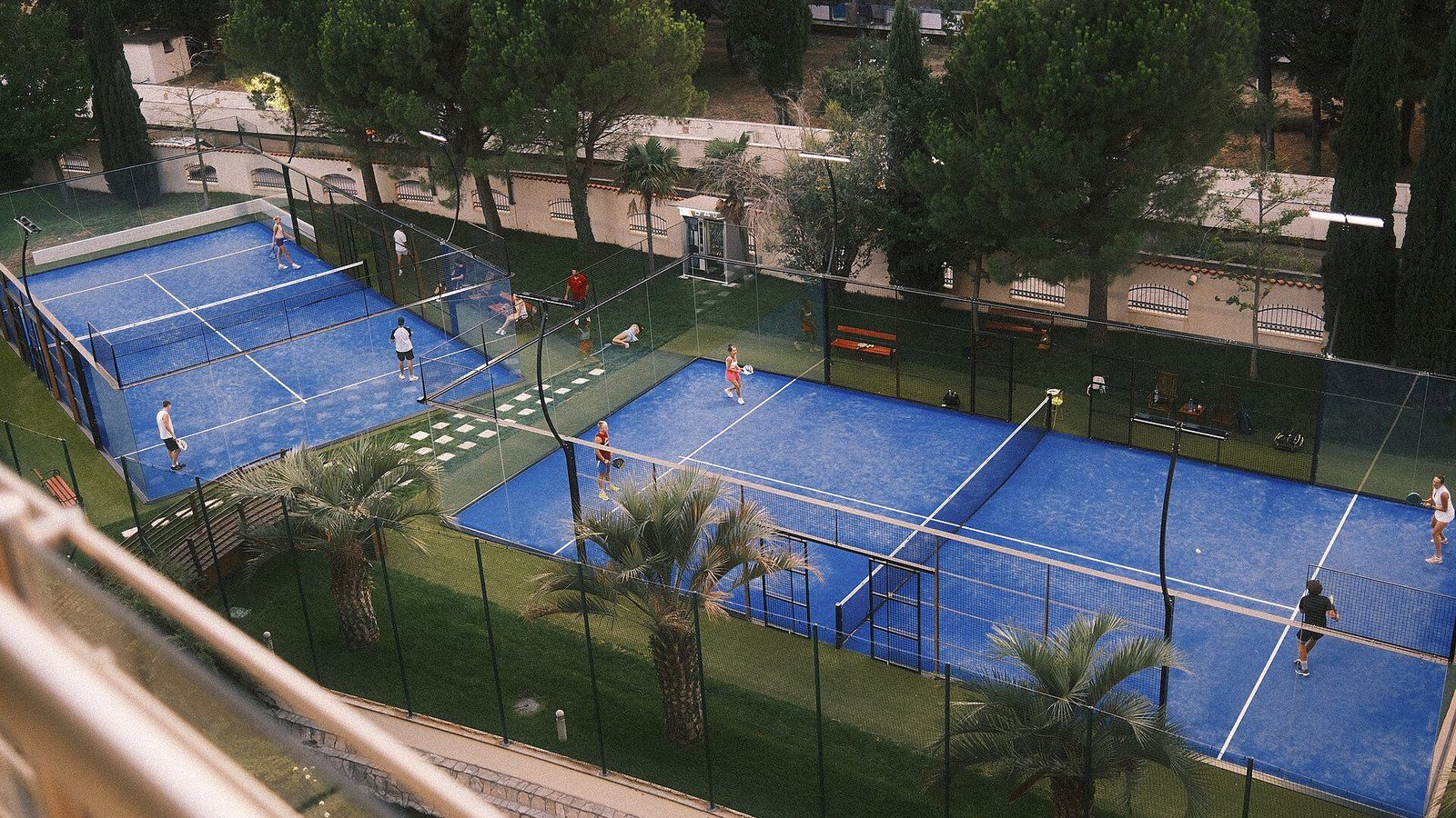 Deux pistes de padel bleues vues d’en haut, entourées de parois vitrées et de grillage, avec des joueurs en double