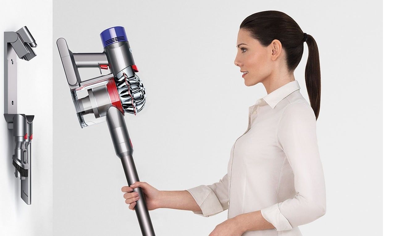 Une femme raccroche un Dyson V8 sur sa station murale