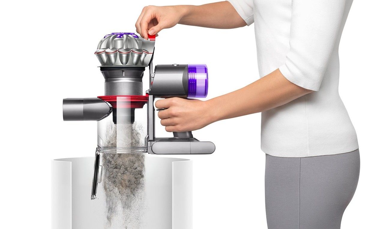 Deux mains vident le bac transparent d’un Dyson V8 au-dessus d’une poubelle